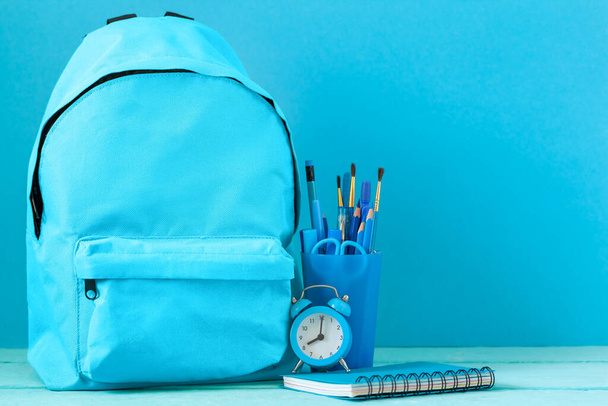 Mochila preparada con artículos de papelería escolar y reloj despertador para la vuelta a la escuela. Concepto azul monocromo color. - Foto, imagen