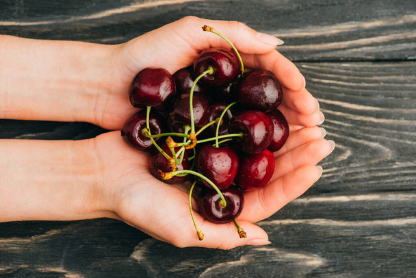 cropped view of woman holding ripe sweet cherries on wooden surface - Foto, afbeelding