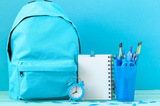 Backpack prepared with empty blank and school stationery supplies, alarm clock for the back to school. Concept blue monochrome color. - Valokuva, kuva