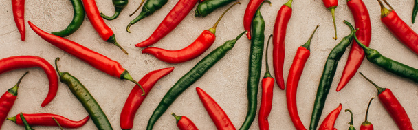 top view of red chili peppers and green jalapenos on beige concrete surface, panoramic shot - Foto, Imagem