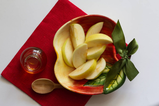 Manzanas cortadas en rodajas en un plato en forma de manzana sobre una servilleta de lino rojo un fondo blanco, frasco con espacio para copiar miel - Foto, imagen