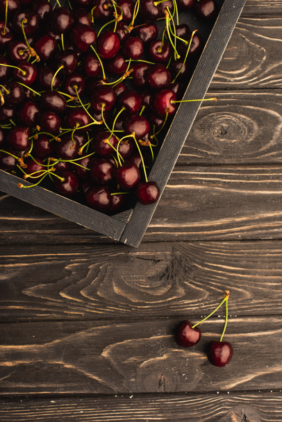top view of ripe sweet cherries in box on wooden surface - Foto, Imagem