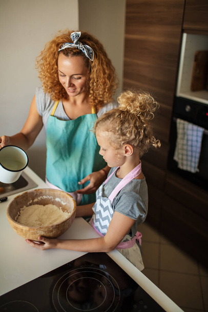 Little daughter helping mother baking in kitchen, family and cooking - Zdjęcie, obraz