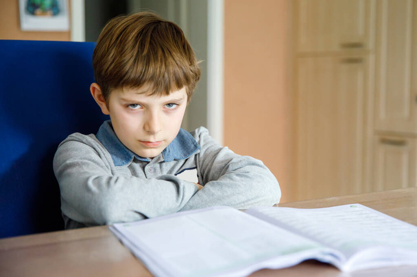 Upset school kid boy making homework during quarantine time from corona pandemic disease. Crying and sad boy frustrating staying at home. - Photo, Image