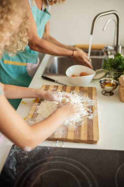 Vrouw en leuke dochter koken op keuken, het maken van deeg voor verjaardagsfeestje. - Foto, afbeelding