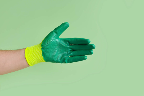 Male hand in a glove for working in the garden, vegetable garden on a green background. Open hand for handshake. - Photo, Image
