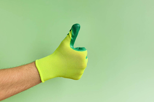 Enseigne les pouces. Main masculine dans un gant pour travailler dans le jardin, potager sur fond vert. Espace de copie. - Photo, image