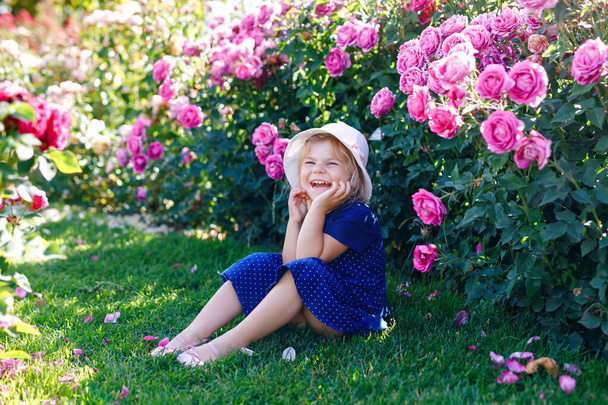 Portrét malé batolátko v rozkvetlé růžové zahradě. Roztomilé krásné krásné dítě baví s růžemi a květinami v parku v létě slunečný den. Šťastné usměvavé dítě. - Fotografie, Obrázek