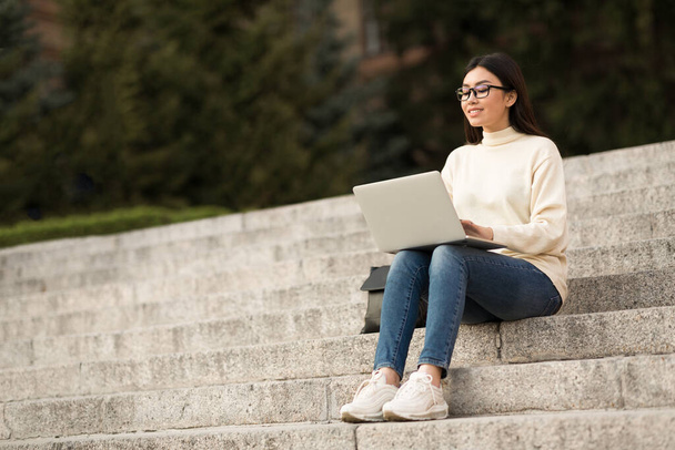 Студент в специальностях с помощью ноутбука, сидящий на ступеньках - Фото, изображение