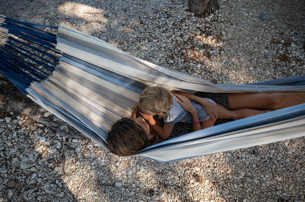 Top view of a loving young mother hanging and relaxing in a hammock with her toddler daughter resting on her. - Фото, изображение