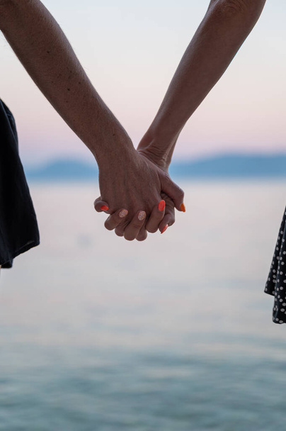 Nahaufnahme des schwulen lesbischen Paares, das am Abend die Hände am schönen Meer hält.  - Foto, Bild