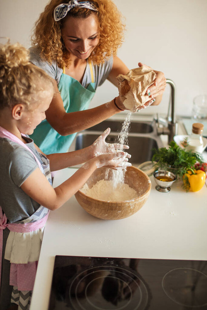 Menina e sua mãe polvilhando farinha em uma tigela e sorrindo ao assar
 - Foto, Imagem