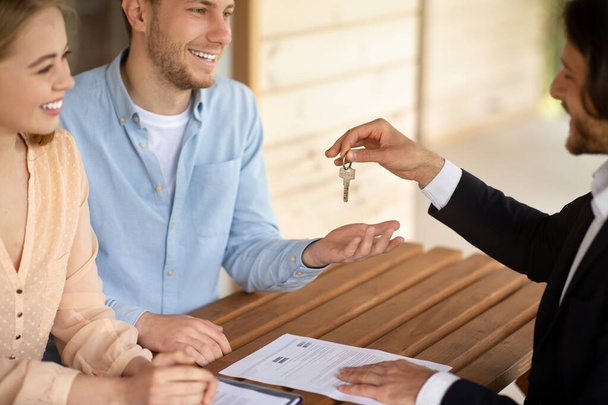 Pośrednik przekazujący klucze do nowego domu szczęśliwej parze małżeńskiej przy stole na świeżym powietrzu - Zdjęcie, obraz