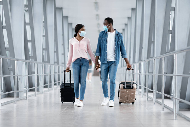 Coronovirus Travels. Black couple in masks walking with luggage at airport building - Фото, изображение