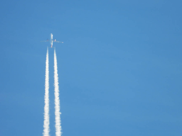 Samolot lecący na przezroczystym błękitnym niebie i kontrastujący z, Silnik spalin kurczy się tworząc z tyłu, Jet kursuje lub szlaki nad niebieskim niebem i chmury. - Zdjęcie, obraz