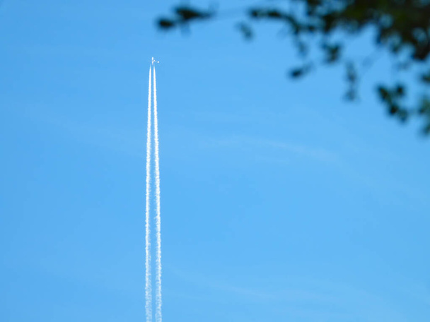 Avión que vuela en el cielo azul claro y contra el que se desvía, las estelas de escape del motor que se forman detrás, las estelas de Jet o las estelas sobre el cielo azul y las nubes. - Foto, imagen