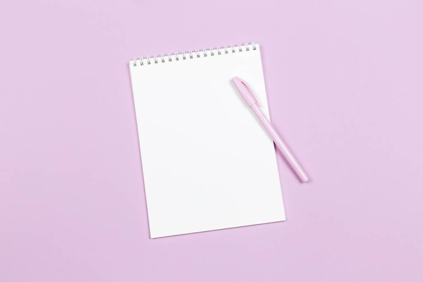 Cuaderno con página en blanco y bolígrafo sobre fondo pastel violeta. Acostado. Lugar para el texto
.  - Foto, imagen