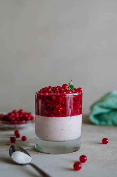 Delicious italian pana cotta with ripe red currant. Fresh healthy dessert in glass with bright berries and mint leaves. Fragrant pannacotta on the table - Fotoğraf, Görsel