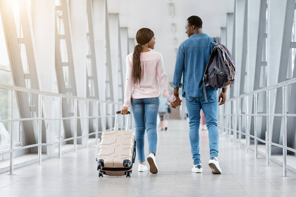 Couple noir romantique marchant avec des valises dans le terminal de l'aéroport, tenant la main - Photo, image