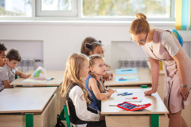 Teacher helping kids with their homework in classroom at school - Fotografie, Obrázek