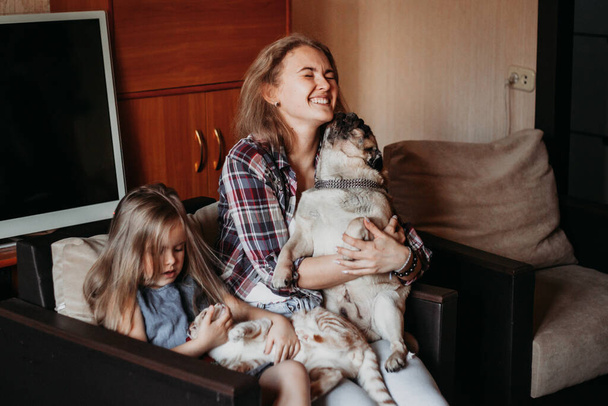 Una mujer, una niña sentada en una silla en casa y sosteniendo a su perro, comunicación con una mascota, familia, preocupaciones y diversión - Foto, Imagen