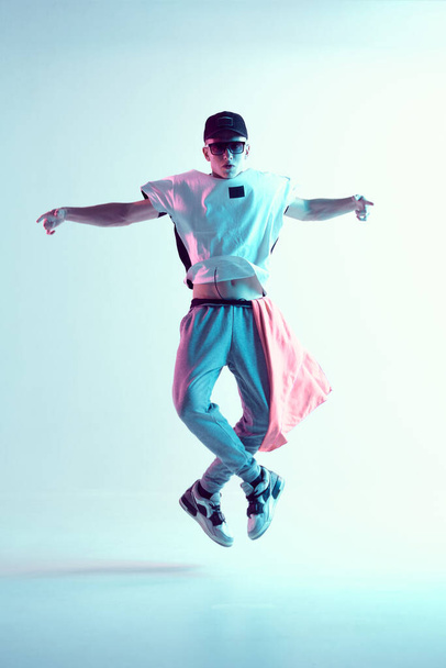 Guy dancing contemporary dance in studio. Neon light blue background. Break dance lessons. - Foto, Bild