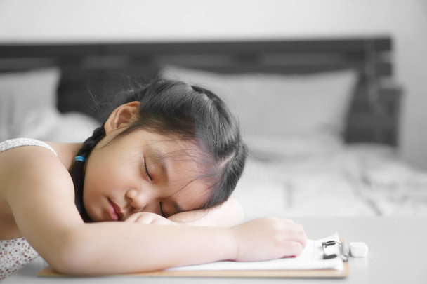 aasialainen lapsi opiskelija tai lapsi tyttö kirjallisesti tai piirtää ja tekee kotitehtäviä tai lukea oppia ja koulutusta kirjoittaa paperille, mutta nukahtaa tai nukkua pöydällä oleskelemalla kotona turvallisesti ja koulun tutkimuksen verkossa makuuhuoneessa - Valokuva, kuva