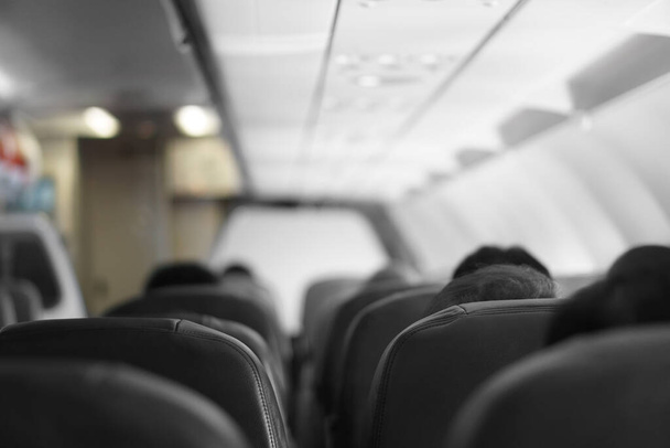 l'intérieur d'un avion ou d'un aéronef avec passagers ou touristes et personnes de dos se dirigent sur des sièges noirs ou une chaise en classe écologique et volant pour le transport ou les voyages et le tourisme de l'aéroport sur prise de vue aérienne - Photo, image