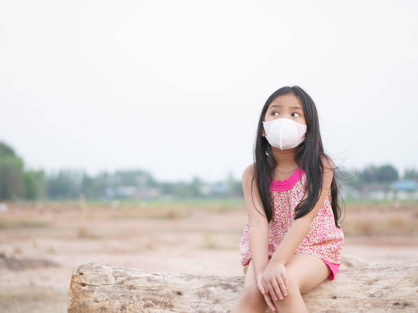 Asian child think new idea or kid girl wear N95 face mask and sick with cold cough sneeze for protect covid 19 virus or PM2.5 dust by smoke or air and close mouth nose to unhappy and look above vacant - Photo, Image