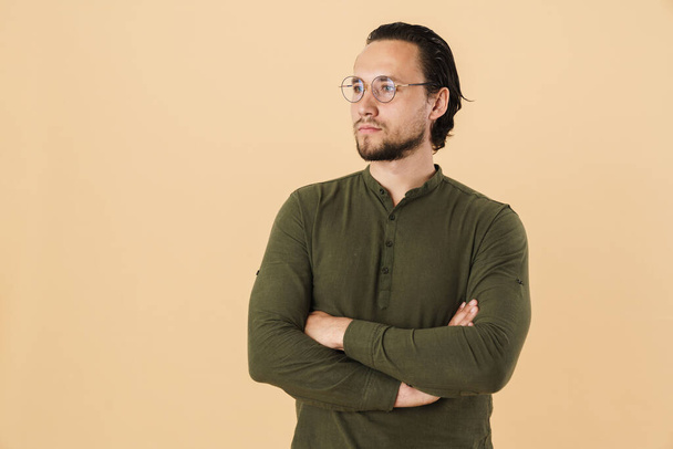 Image of young confident man wearing eyeglasses looking aside at copyspace isolated over beige background - Foto, immagini