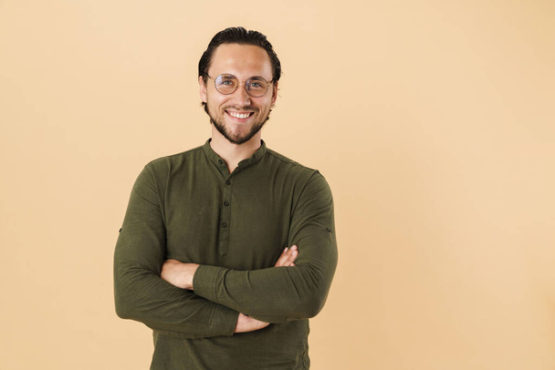 Image of young happy man wearing eyeglasses smiling and looking at camera isolated over beige background - Fotografie, Obrázek