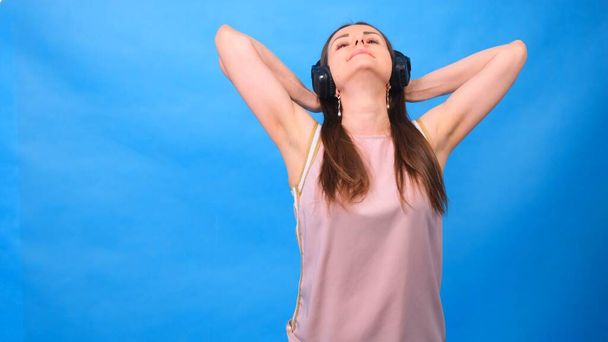 Portrait of a cheerful happy girl student with listening to music with headphones and dancing isolated over a blue background - Photo, Image