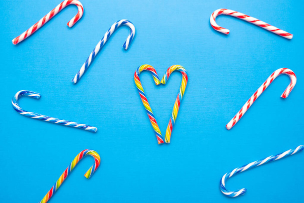 muchos bastones de caramelo multicolores y un corazón sobre un fondo azul, espacio de copia
 - Foto, Imagen