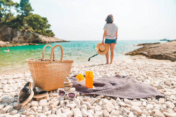 соломенная шляпа и сумка с ластами и солнцезащитный крем на берегу моря женщина на заднем плане - Фото, изображение