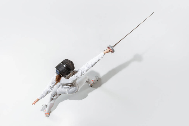 Teen girl in fencing costume with sword in hand isolated on white background, top view - 写真・画像