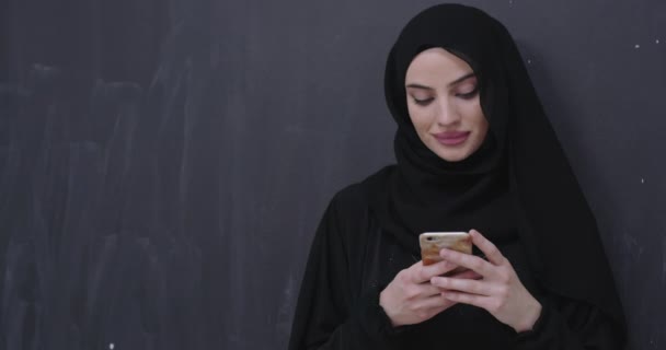 young modern muslim business woman using smartphone wearing hijab clothes in front of black chalkboard - Footage, Video