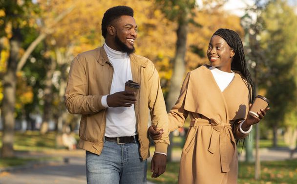 Joven pareja afro tomando café mientras camina en el parque de otoño - Foto, Imagen