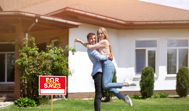 Люблячий чоловік тримає свою щасливу дружину з ключем будинку біля їх нової власності, вільний простір
 - Фото, зображення