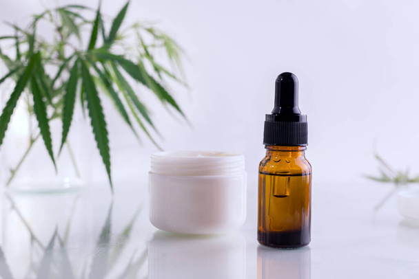 Natural cosmetics with cannabis oil. Mockup with a White clean jar with cosmetics cream and fresh green leaves of hemp. - Photo, Image