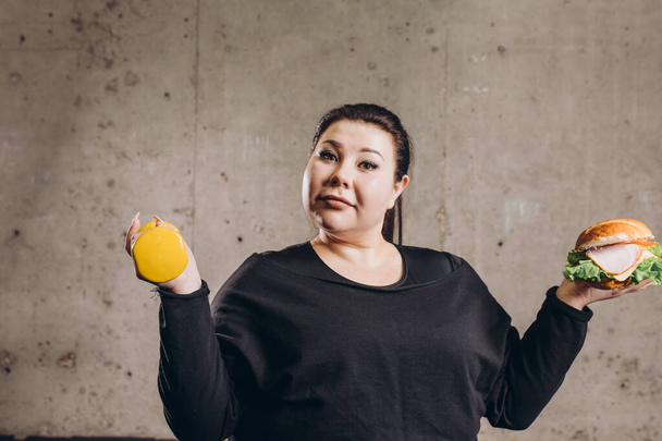 obese beautiful woman with sport device and hamburger looking at the camera - Fotografie, Obrázek