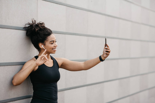 Спортивный блогер на тренировке. Счастливая девушка с фитнес-трекером делает селфи на смартфоне - Фото, изображение