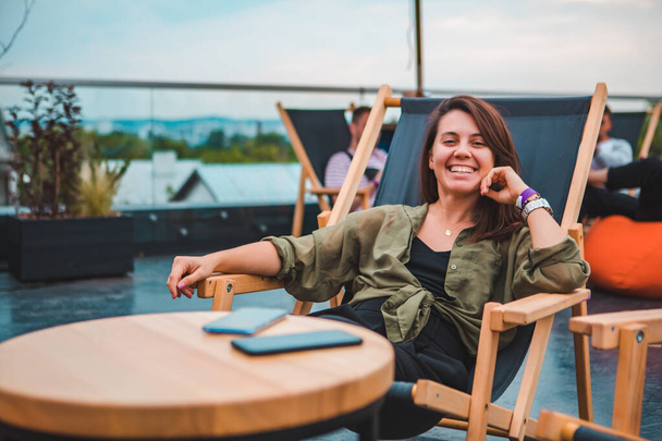 young gorgeous woman sitting in cozy chair at outdoors cafe looking at camera - Foto, Bild