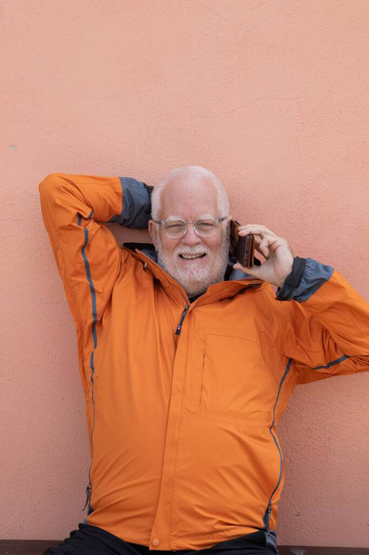 Siwowłosy starszy mężczyzna w pomarańczowej kurtce rozmawiający przez telefon komórkowy - Zdjęcie, obraz