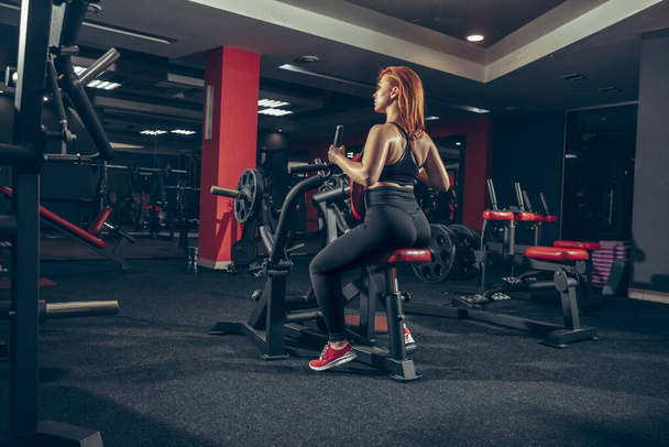 Young muscular caucasian woman practicing in gym with equipment. Wellness, healthy lifestyle, bodybuilding. - Foto, Imagen