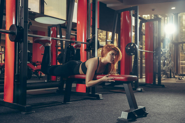Young muscular caucasian woman practicing in gym with equipment. Wellness, healthy lifestyle, bodybuilding. - 写真・画像
