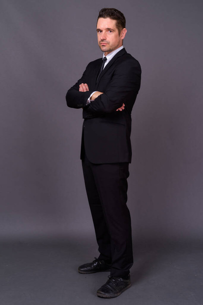 Studio shot of handsome bearded businessman in suit against gray background - Photo, Image