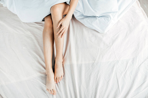 top view photo. girl is massaging her legs while lying on the bed - 写真・画像