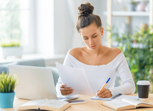 Focused young businesswoman studying online, watching webinar, podcast on laptop, making notes, sitting at work desk. E-learning concept. - 写真・画像