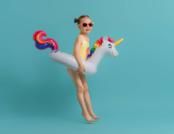 Happy child wearing swimsuit. Girl with swimming ring unicorn. Kid on a colored turquoise background. - Foto, immagini