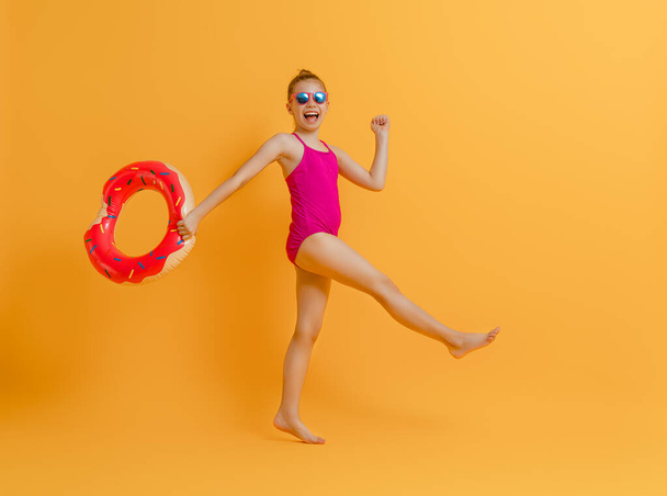 Happy child wearing swimsuit. Girl with swimming ring donut. Kid on a colored yellow background. - Foto, Imagem